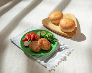 Two fried cutlets on a plate with fresh vegetables, with hamburger buns