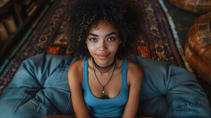 Fototapeta premium Rest Concept. Above top view of happy black lady sitting on bean bag at home in living room. Cheerful casual woman relaxing on sofa leaning back, enjoying free time, banner panorama, free space mockup