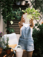 An individual holding a plant in front of their face, surrounded by greenery and plant pots The focus is on the potted plant