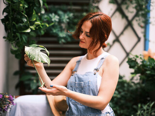 A woman examines a variegated leaf of a houseplant, appreciating its details on her balcony garden