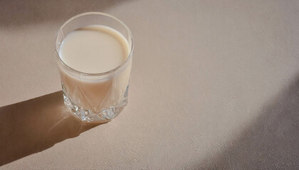 A glass of milk standing on a beige countertop next to ears of wheat, illuminated by the sun's rays, boho style. Szklanka mleka stojąca na beżowym blacie obok kłosów pszenicy w boho stylu. - obrazy, fototapety, plakaty