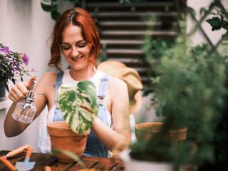 Contented woman in overalls using a mist spray bottle on a plant among her balcony garden
