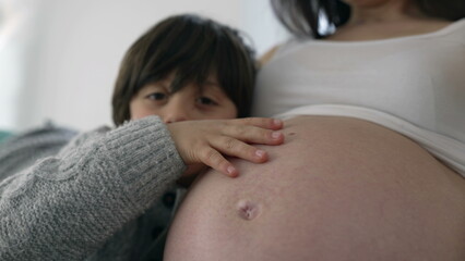 Heartwarming moment of 5 year old boy gently kissing mother's belly during late stage pregnancy,...