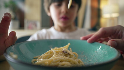 Pasta dish close-up of fork and rich carb food, kid's plate with small boy in blurred background