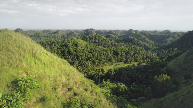 Philippines countryside aerial: mist farmlands with people at hillside valley. Rural ground road near farm admist green tropical grassy mounts. Amazing Filipino lands scape at cloudy day. Soft shot
