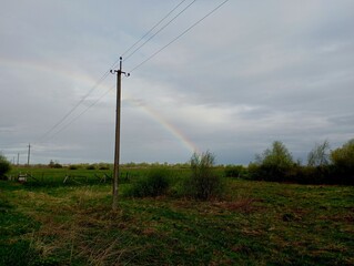 A beautiful rainbow in the sky over a power line in spring. Beautiful landscape with a rainbow in the countryside.