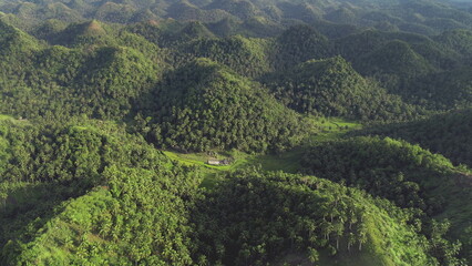 Philippines green jungle mountains aerial view. Small farm building at hillside grassy valley. Asian tropical rural scenery. Nobody Filipino tropic nature landscape in cinematic drone shot