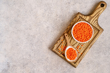 Red lentils in ceramic bowl and spoon on wooden board. Top view