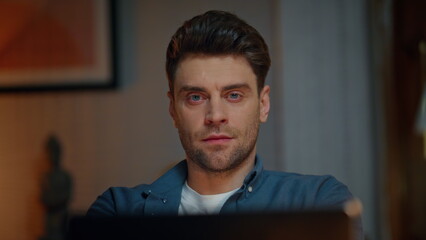 Relaxed man looking laptop at night workplace closeup. Guy stretching arms alone