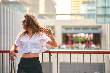 A woman in casual attire is walking with her hair flowing in the sunlight with urban background