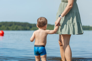 small child with mom on the beach, protecting the baby's skin from the sun while swimming in the water in summer