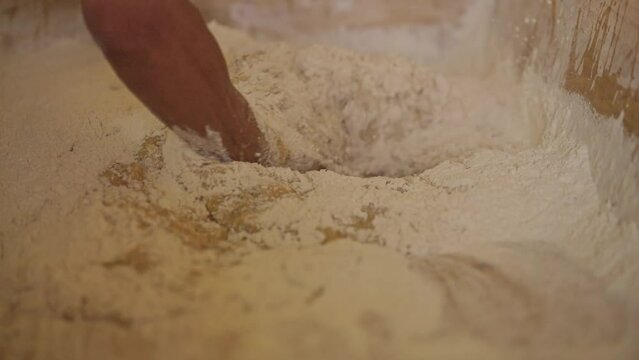 Close-up shot of hands integrating raw ingredients for making wheat flour dough.