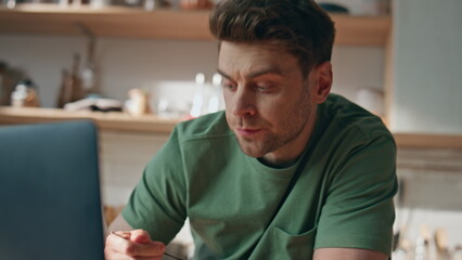Eating guy looking computer enjoying breakfast in kitchen closeup. Man in home