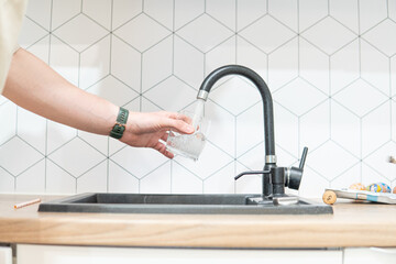 Pouring water from the tap into a glass. Hydrating with tap water, emphasizing hydration care.