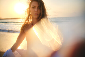Fototapeta na wymiar A serene photo of a woman on the beach during sunset, with sunlight creating a lens flare effect