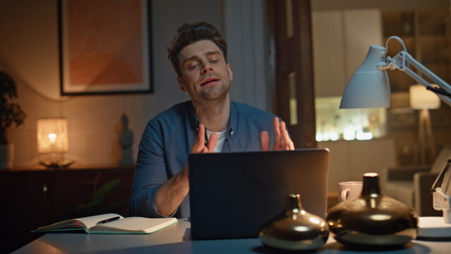 Emotional man explaining online meeting laptop sitting night workplace closeup