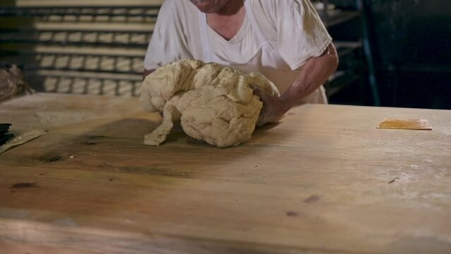 Latin baker manipulates a portion of dough on a wooden table.