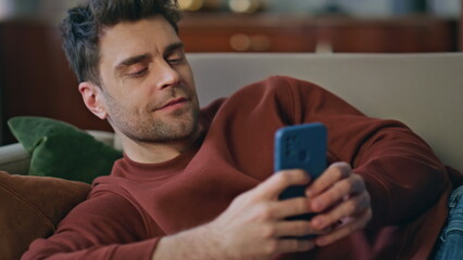 Chilling man messaging cellphone lying on apartment couch close up. Smiling guy