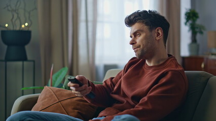 Nervous guy switching television channels on couch with controller close up.