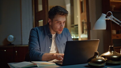 Focused man staring computer reading email at dark flat closeup. Excited winner