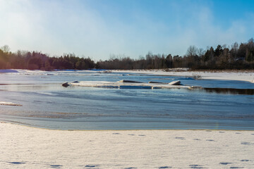 Snow and ice of a forest lake melt under the warm rays of the sun. Spring landscape warming season