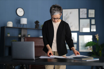 A professional businesswoman diligently manages paperwork at her office desk, showcasing confidence...