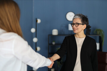 In a professional setting, a businesswoman and her colleague share a handshake, symbolizing...