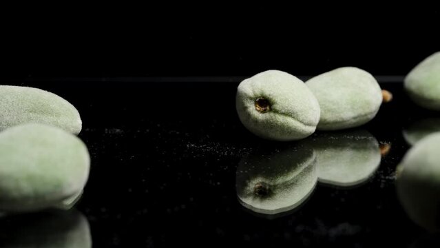 A green unripe almond falls and shatters on a black table. Slow motion.