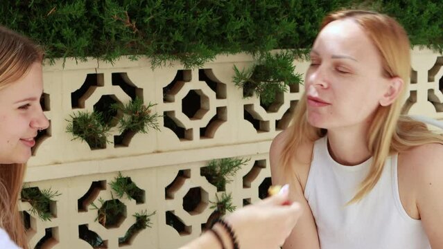 Teenage daughter feeds her mother churros while sitting at table outdoors. concept of happy family. Churros, delicious and typical sweet of Spain.