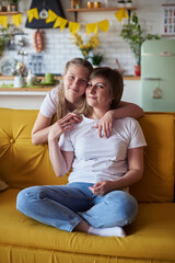 Mom and daughter hugging on the couch on Mother's Day looking at the camera
