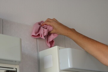 Person cleaning bathroom tiles with a cloth.
