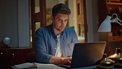 Smiling businessman browsing computer texting email at cozy dark flat closeup