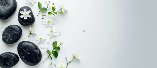 Smooth black spa stones and delicate white flowers arranged on a pristine white background