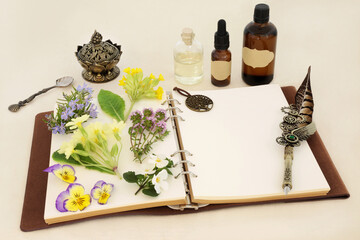 Homeopathic herbal medicine preparation with spring flowers, herbs and essential oil bottles with notebook and quill pen. Natural floral concept for flower essences on hemp paper.