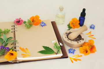 Flowers and herbs for naturopathic, medicinal and aromatherapy treatments. Herbal medicine ingredients for alternative remedies with recipe notebook on hemp paper background.