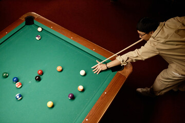 Minimal top view of Asian man playing billiards and hitting ball with cue stick copy space