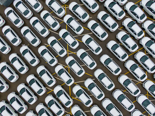 A large parking lot full of white cars. Cars leaving the car factory are waiting at the port for...