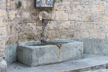 Stone fountain in Lugano, with water flowing and surrounded by natural scenery.