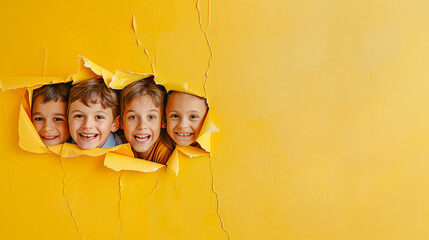 Cheerful children peering out from behind a yellow solid background with copy space