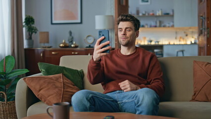Joyful hipster waving web camera smartphone at home. Smiling guy video call