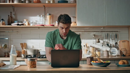Pensive freelancer texting laptop at home kitchen closeup. Man eating breakfast