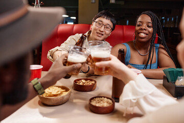 Diverse group of friends clinking beer bottles and cheering sitting at diner table