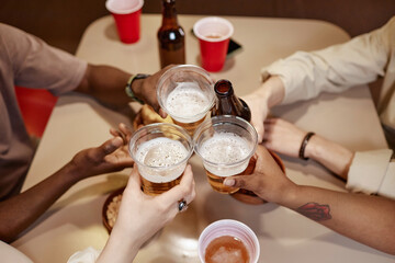 Top view of multiethnic group of people clinking beer cups over table in cafe or diner
