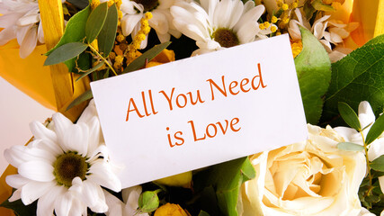 All you need is love slogan written on a business card on a background of flowers