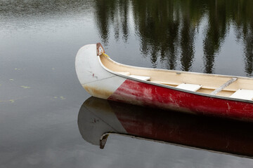 Red and white canoe on a calm lake with reflections of the forest
