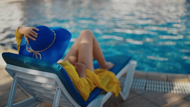 Woman in blue hat is relaxing near the pool.
