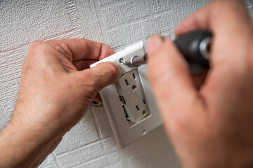 Installation or repair of electrical outlet socket box within the wall. Serviceman or repairman fixing with Type B Duplex Receptacle - American socket with grounding