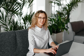 young focused freelancer working with notebook in cafe, typing text and smiling, concentrated caucasian blonde businesswoman in white shirt, green plants in background, freelance concept