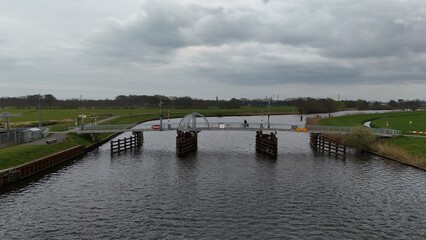 Serene river landscape with a modern pedestrian bridge connecting green embankments under a cloudy sky, reflecting a tranquil and scenic natural environment.