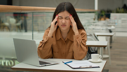 Stressed tired Asian woman working in cafe with laptop paperwork problem business difficulty sick...